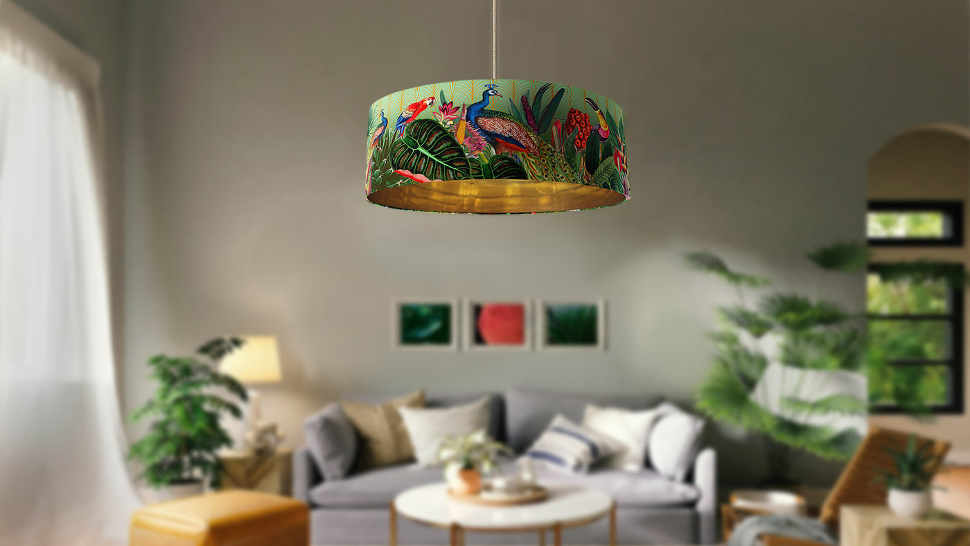 It's written "Colourful Lampshades bring elegance and joy  to your home" with blurred background picture showing the art deco tropicana lampshade with gold lining as a ceiling pendant in a living room setting, with tropical style decor